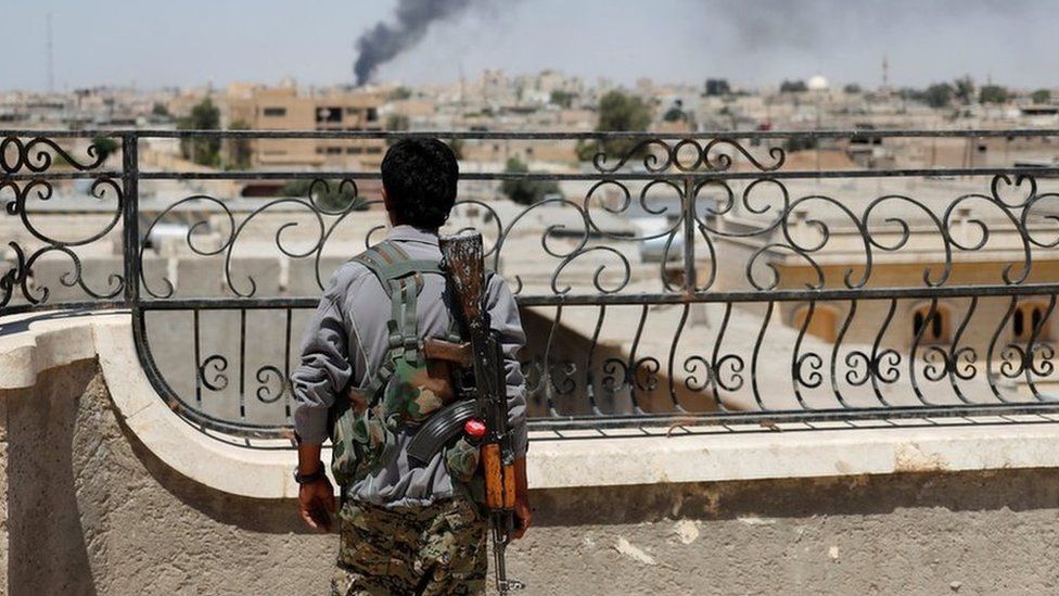 A Kurdish fighter looks across Raqqa after a coalition airstrike