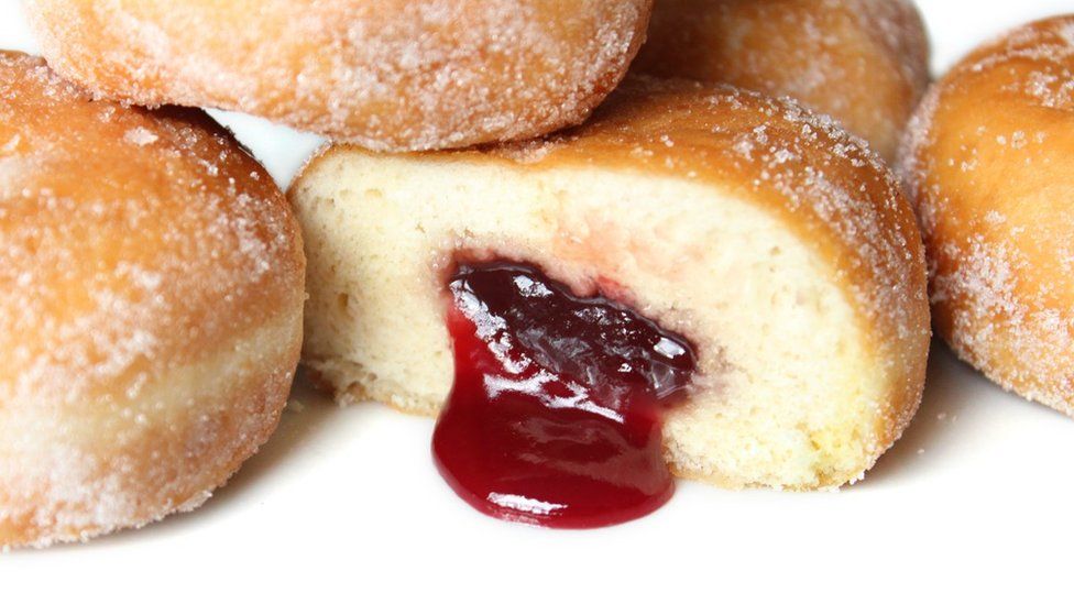 Pile of jam doughnuts with one of them cut in half with red jam oozing out