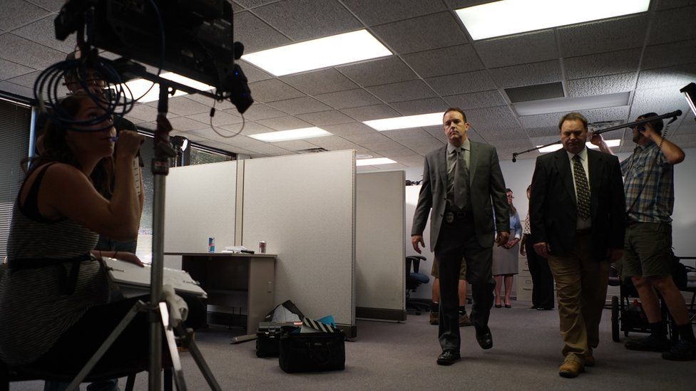 Behind-the-scenes shots shows actors as detectives being filmed by crewmembers
