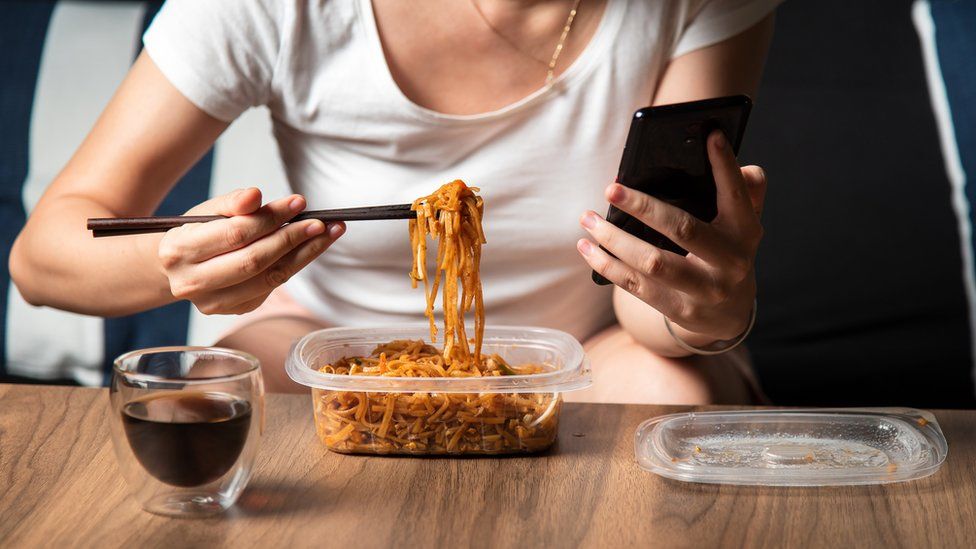 Woman eating takeaway noodles from plastic box