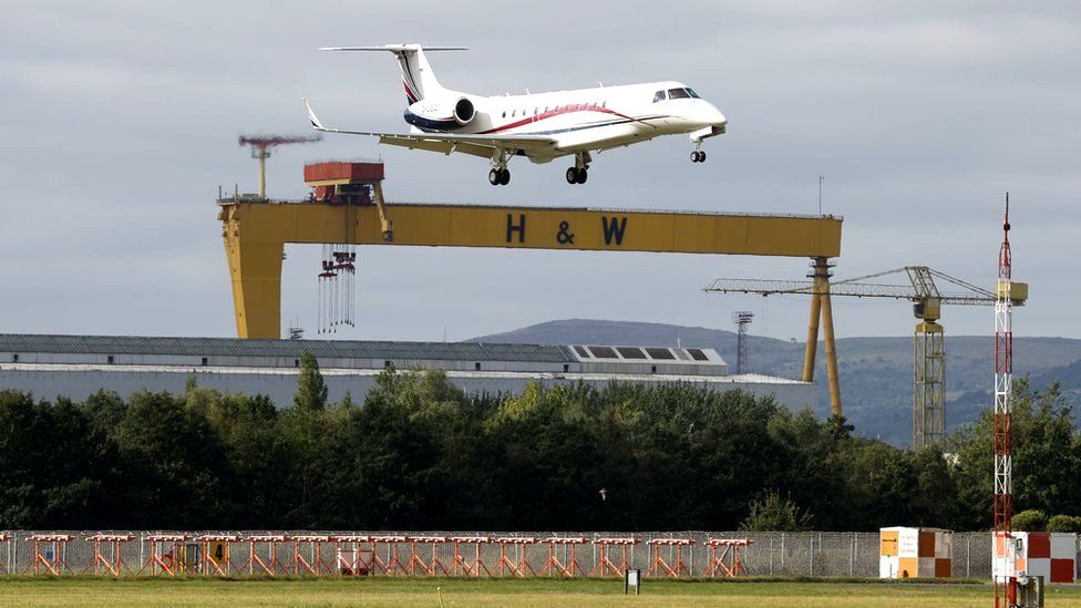 A plane carrying King Charles and Camilla, the Queen Consort, prepares to land at Belfast City Airport, with a Harland and Wolff shipyard crane in the background