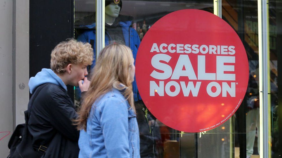 Shoppers walk past a sale sign in a store on Oxford Street in central London as the winter sales begin