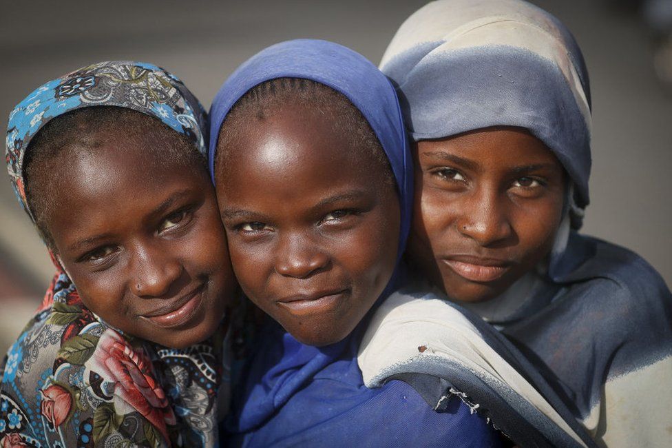Three girls hug each other and smile.