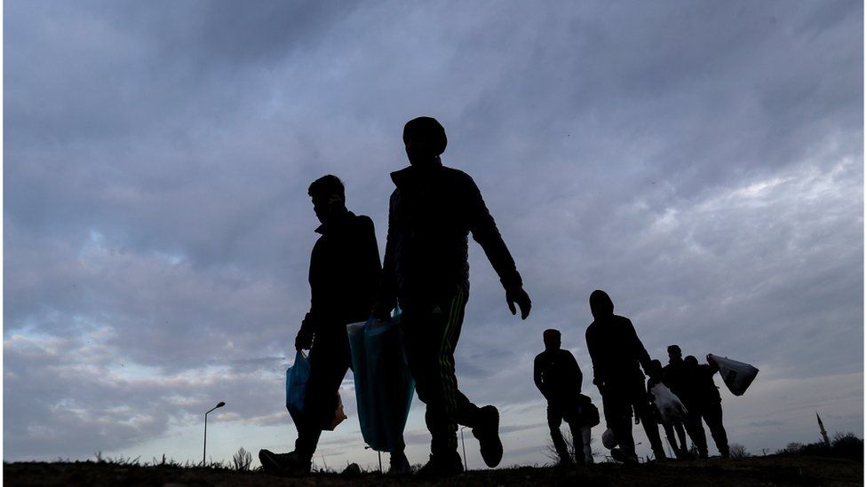 A silhouetted group of migrants and refugees
