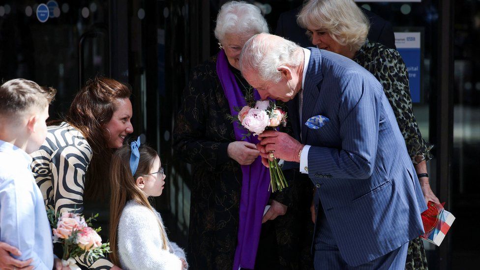 The King receives flowers from a young person outside the hospital