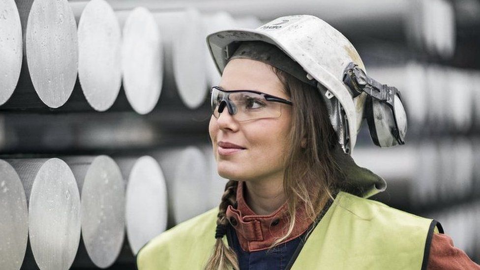 Female Norsk Hydro worker standing in front of aluminium tubes