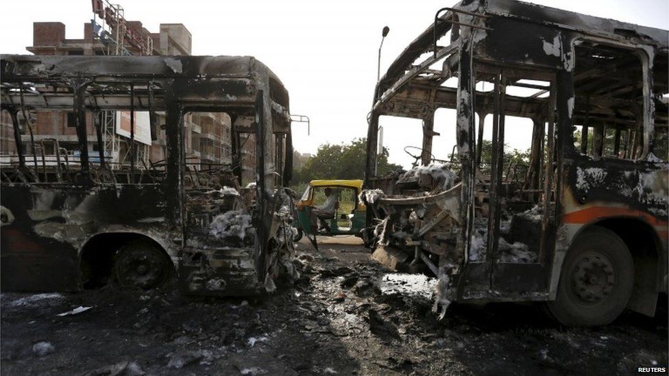 An auto rickshaw moves past damaged passenger buses which were burnt in Wednesday's clashes between protesters and police in Ahmedabad, India, August 27, 2015