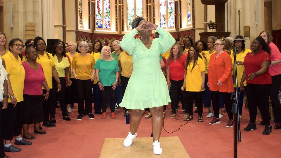 Singers in multicoloured clothes being led by their chorus leader