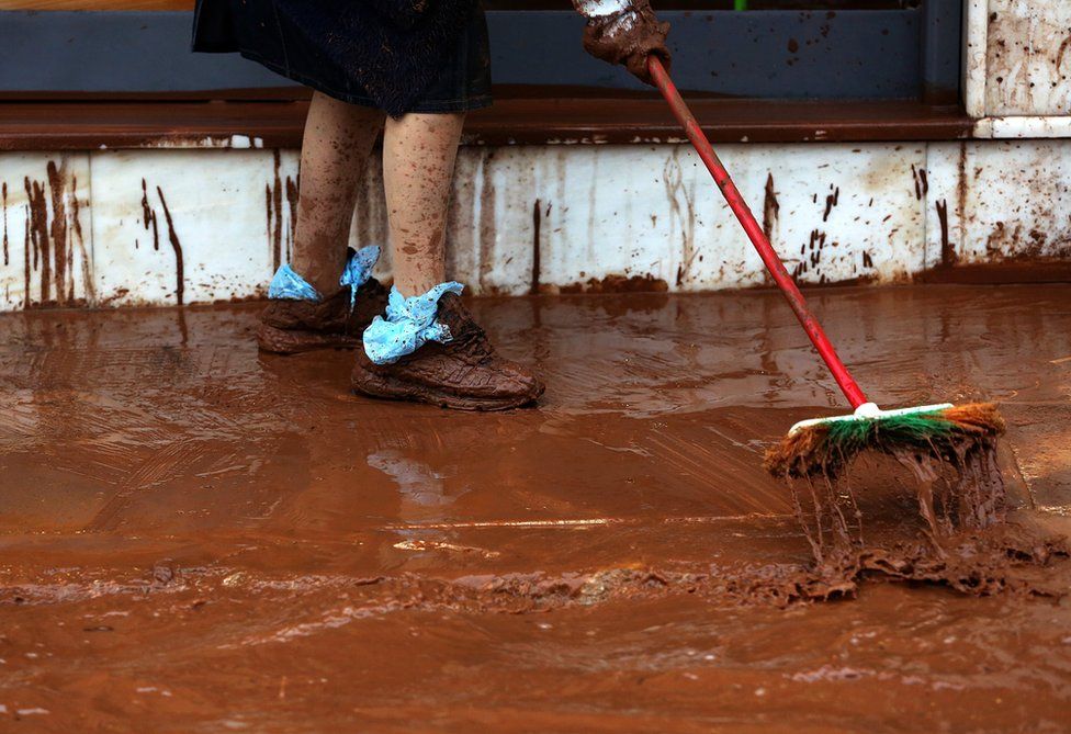 A woman sweeps mud outside her house.