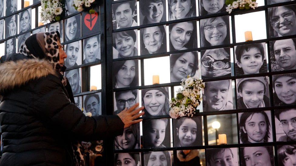 Фотография женщины у мемориала в Торонто в 2022 году с видом на фотографии некоторых жертв рейса 752.
