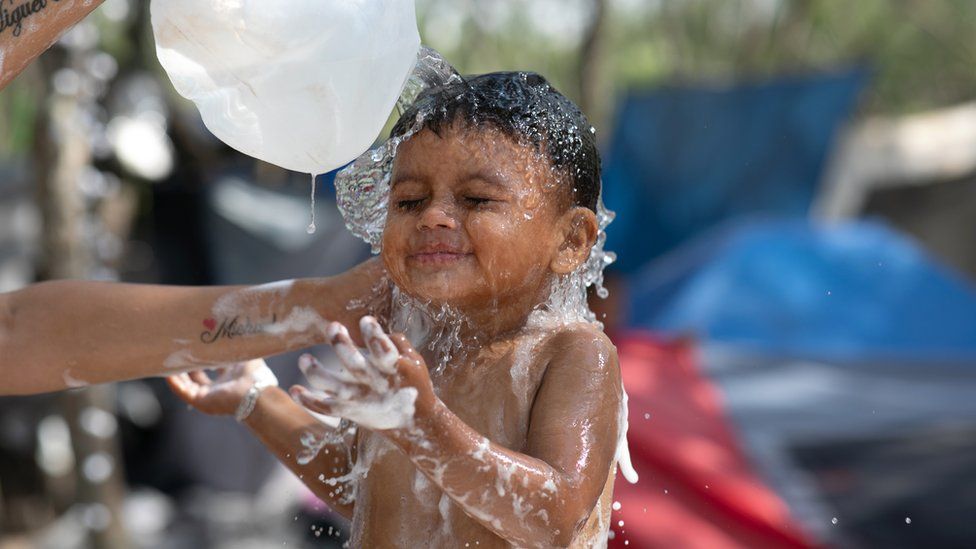 Child at a migrant camp enjoying being splashed with water