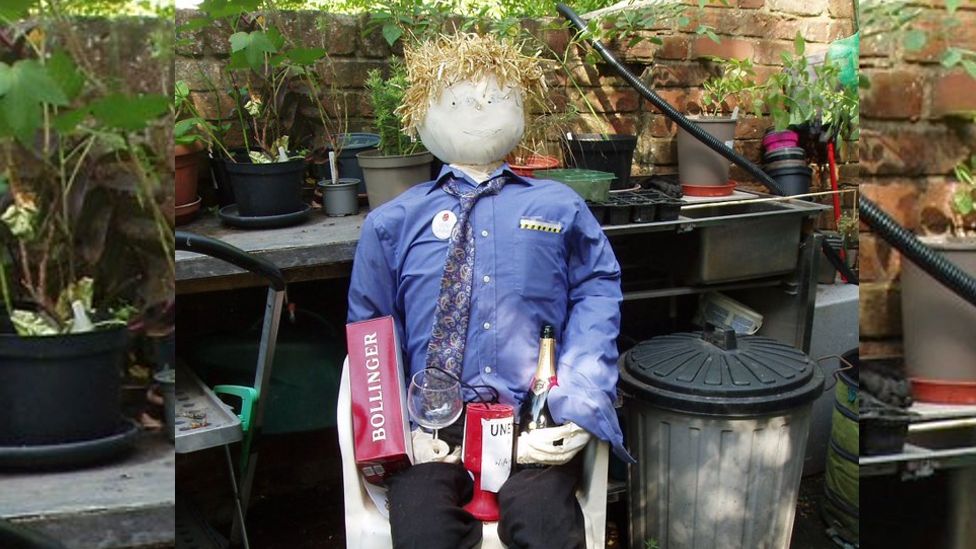 The scarecrow featuring straw hair, a bottle of champagne, a fixed penalty notice and a charity donation box.