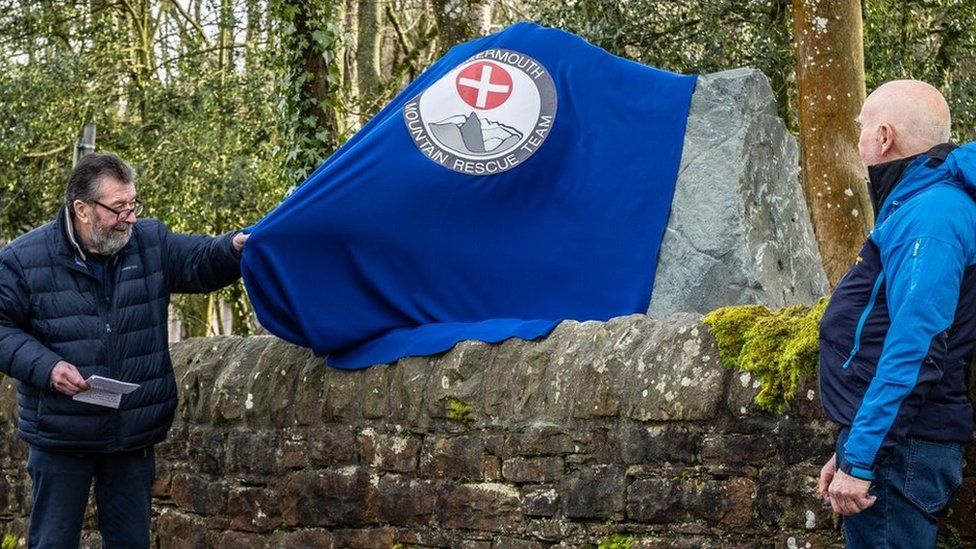 A man pulls a blue cloth away to reveal a large stone sign