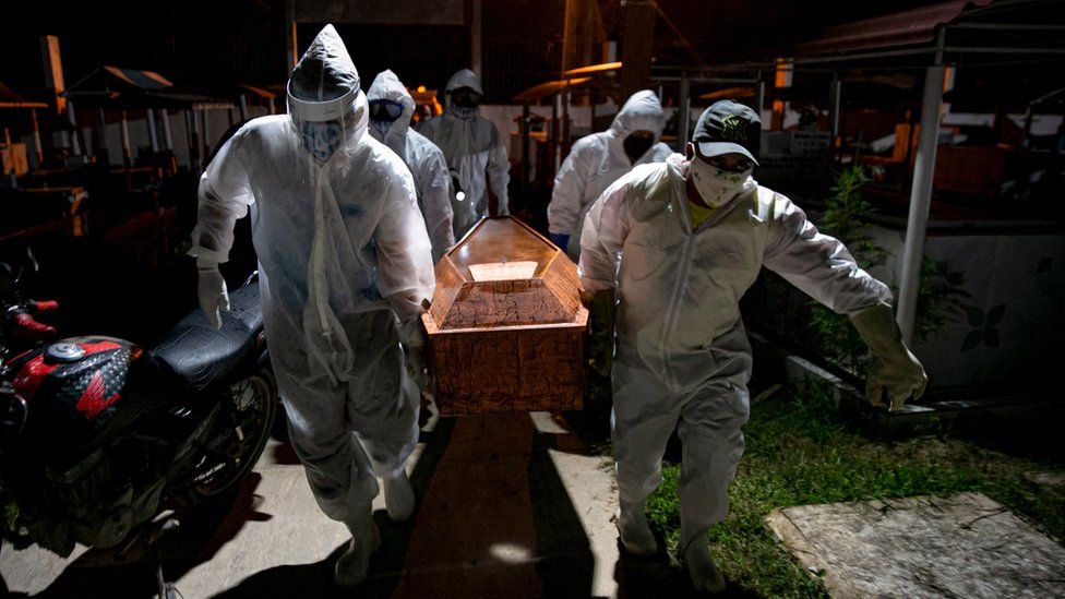 Gravediggers wearing protective clothing carry the coffin of a victim of the coronavirus