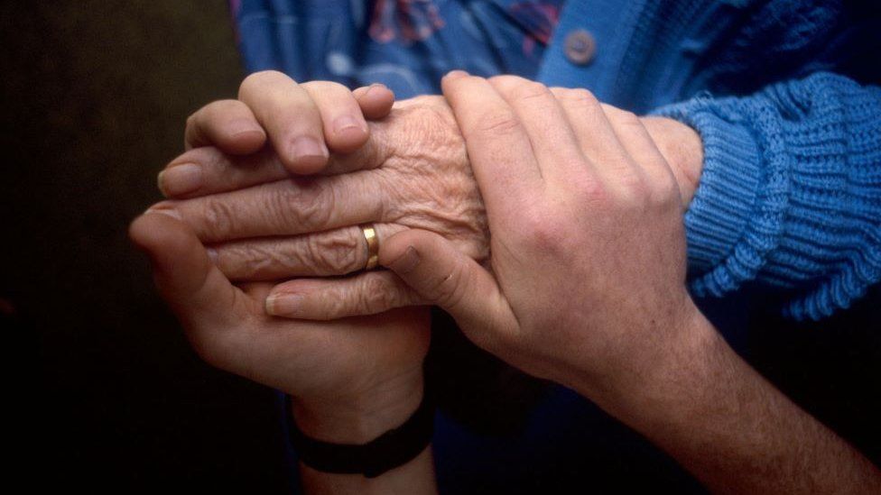 Health carer holds the hand of an elderly patient.