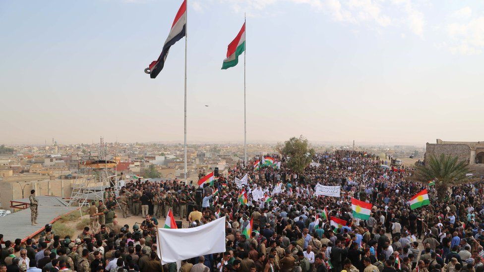 Thousands of Iraqis in Kirkuk wave Kurdish flags at an open-air rally supporting independence, accompanied by armed men.