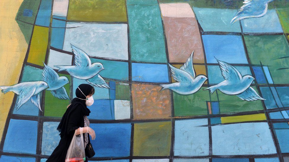An Iranian women walks past a colourful wall in the capital Tehran