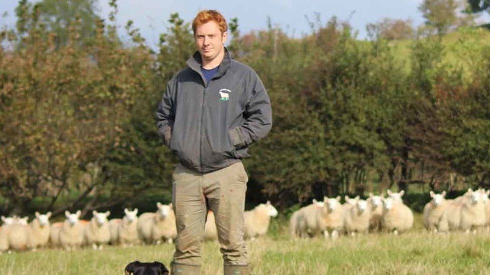 Мэтт в своем фермерском снаряжении с овцами на заднем плане