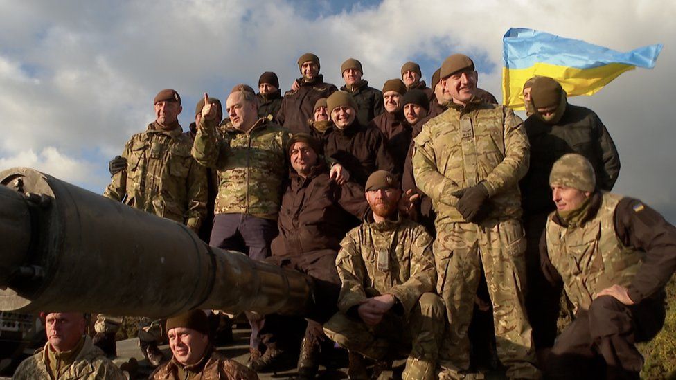A group of Ukrainian soldiers stand in front of a Ukrainian flag