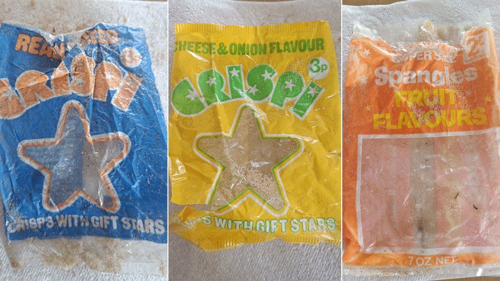 A blue empty packet of ready salted crispi, crisps with gift stars; a yellow empty packet of cheese and onion crispi, crisps with gift stars; an empty orange packet of fruit flavour spangles