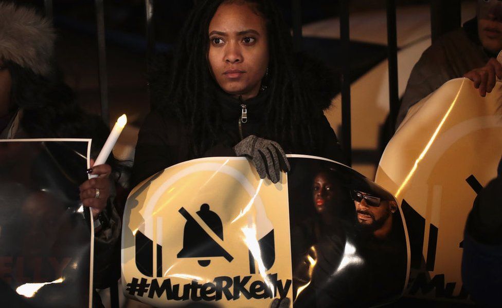 A protester holding a #muteRKelly banner