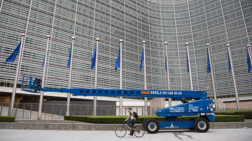 A man rides his bike past EU flags in front of EU headquarters in Brussels on Friday, June 24, 2016