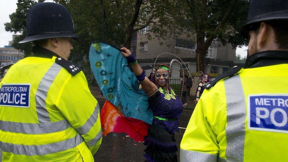 Police officers look on as members of the London Samba School perform during the parade at Notting Hill Carnival
