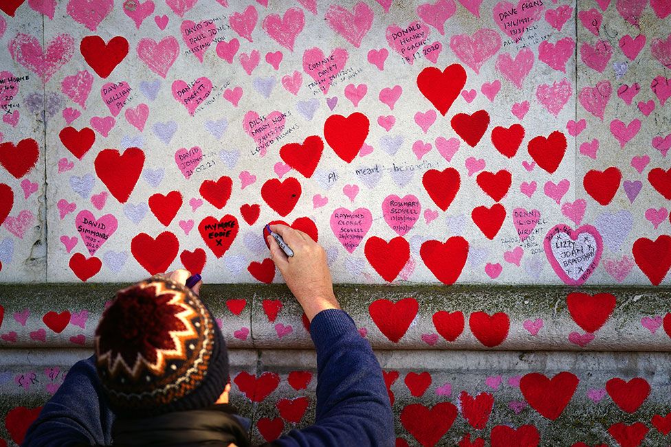 A man writes on a heart at the National Covid Memorial Wall, in Westminster, London on 13 January 2022