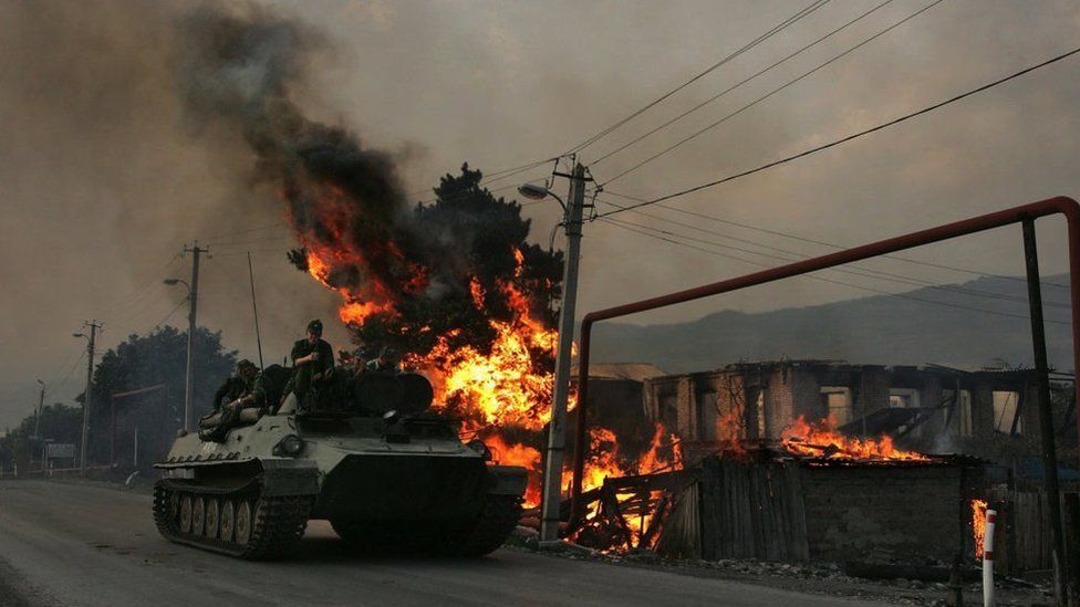 A Russian armoured troop-carrier moves with soldiers atop next to a house set on fire by South Ossetian militia on August 18, 2008 in the Georgian village Kvemo-Achebeti
