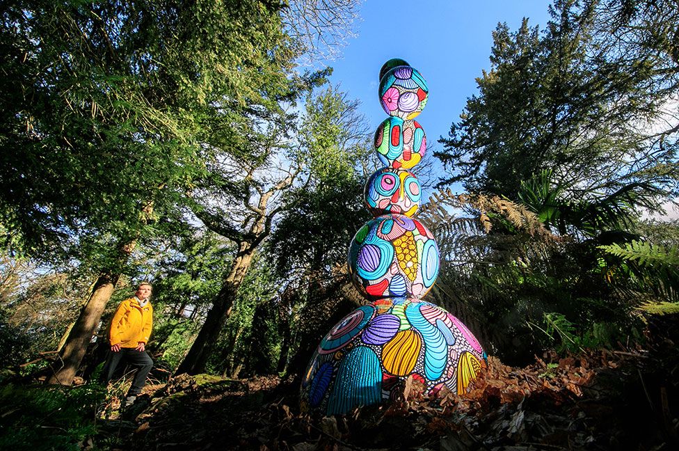 A person looks at a colourful sculpture in a woodland