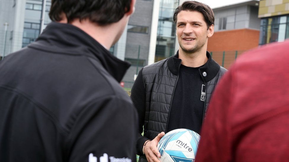 George Friend holds a football and talks to some people