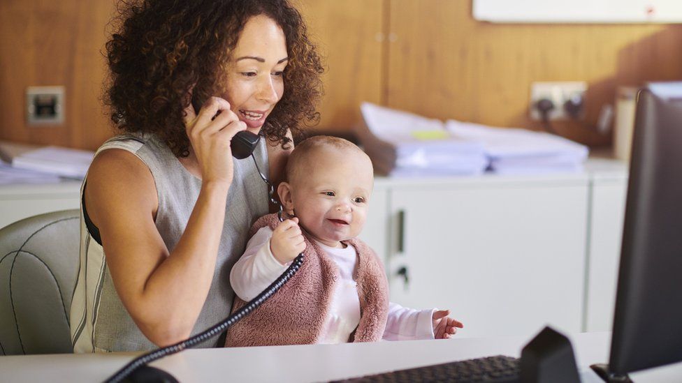 Woman on the phone in front of a computer with a baby on her lap