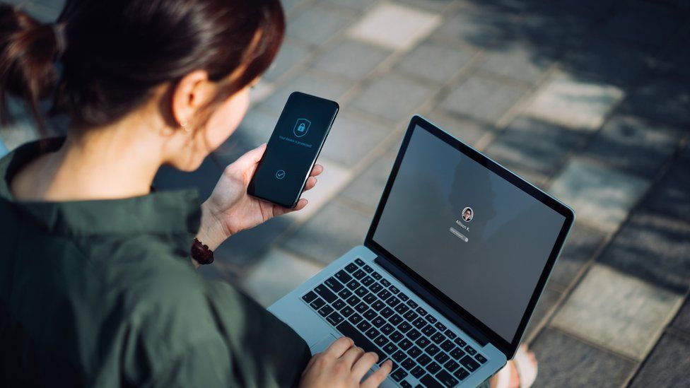 A woman using a laptop and using her smartphone for two-factor authentication