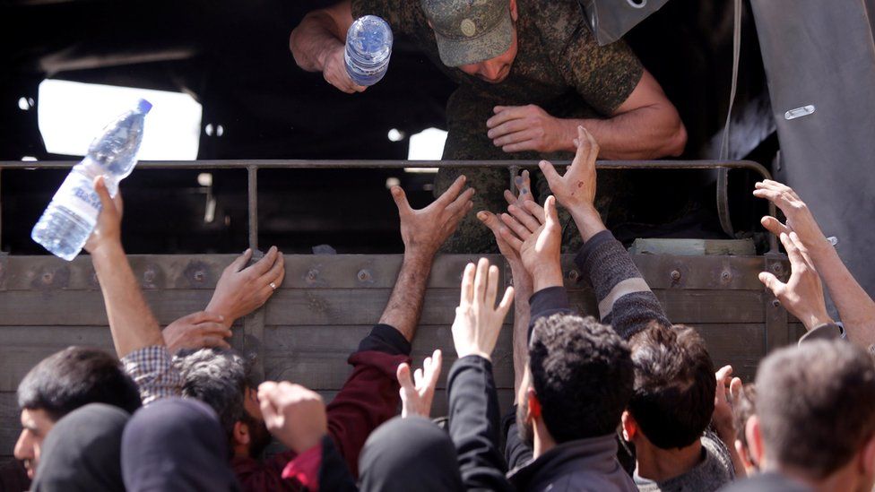 A Russian soldier distributes water to civilians who have fled the Eastern Ghouta, at a shelter in Adra, near Damascus, (20 March 2018)