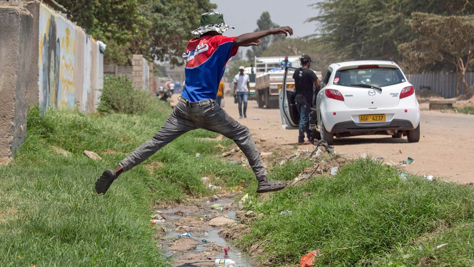 A man jumps over a storm water drain with flowing sewage in Chitungwiza, Zimbabwe, 9 October 2023