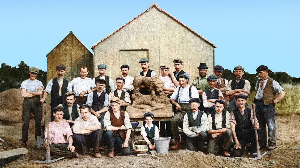 A group of men and boys standing with uncovered stone lion