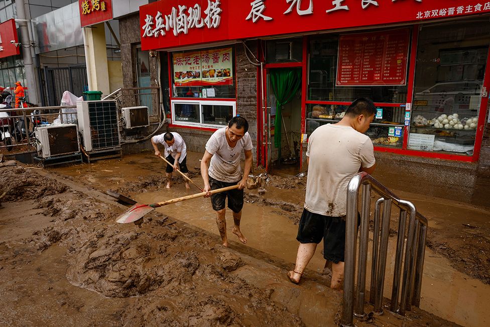 Men shovel mud outside a store in Mentougou District, west of Beijing, China, 01 August 2023. Heavy rains brought by Typhoon Doksuri caused floods in northern China and left two dead and thousands being evacuated as Beijing experienced its heaviest rainfall of the year.