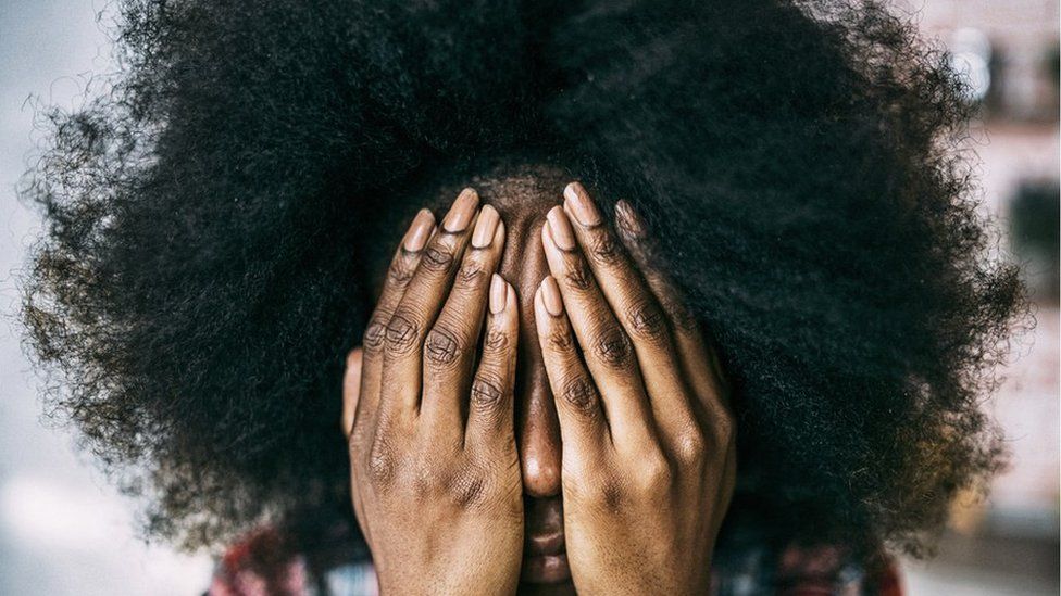 A black woman covers her face with her hands