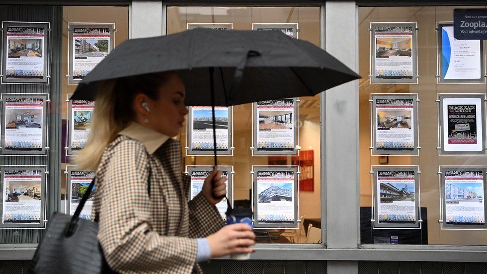 Woman with umbrella walks past estate agents