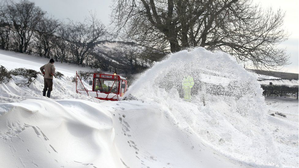 A homeowner watches over a snowblower as it clears the road which leads to the hamlet of Parkhead near Kirkoswald, Cumbria