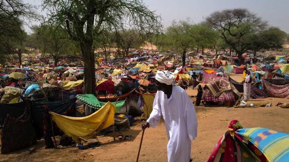 Суданский мужчина ходит с тростью среди тысяч красочных палаток посреди пустыни.