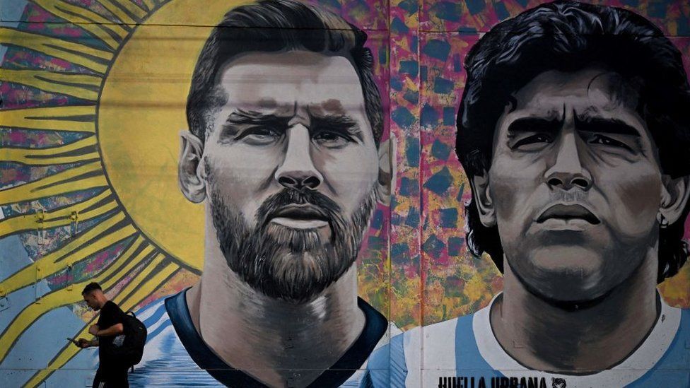 A man walks past a mural of Lionel Messi and Diego Maradona