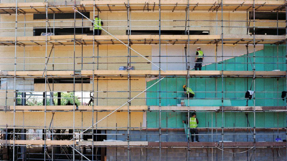 Workers cladding external wall from scaffolding