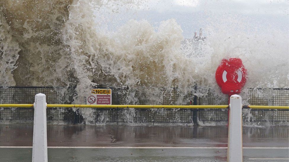 A wave crashes over a barrier next to a road