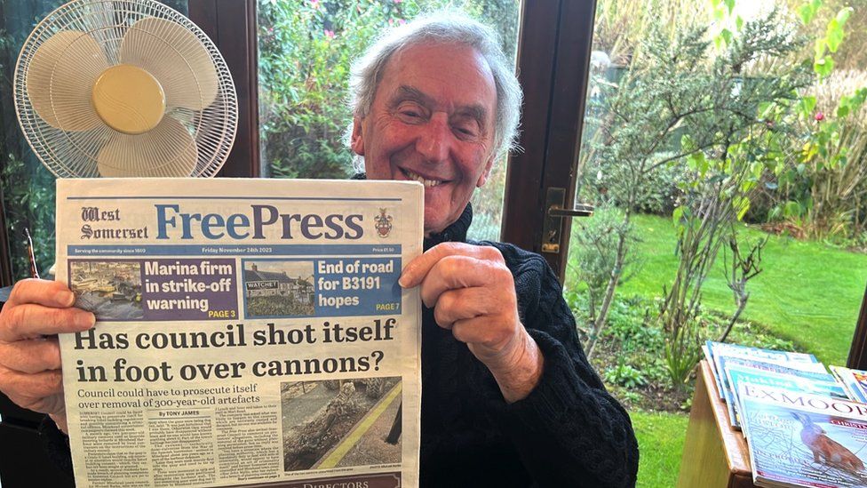 Image of Tony James. He is holding a copy of the West Somerset Free Press and smiling.