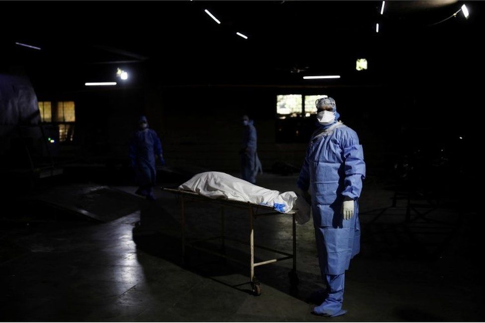 A health worker wearing personal protective equipment (PPE) stands next to the body of a man, who died from the coronavirus disease (COVID-19), before his cremation, at a crematorium in New Delhi, India April 21, 2021.