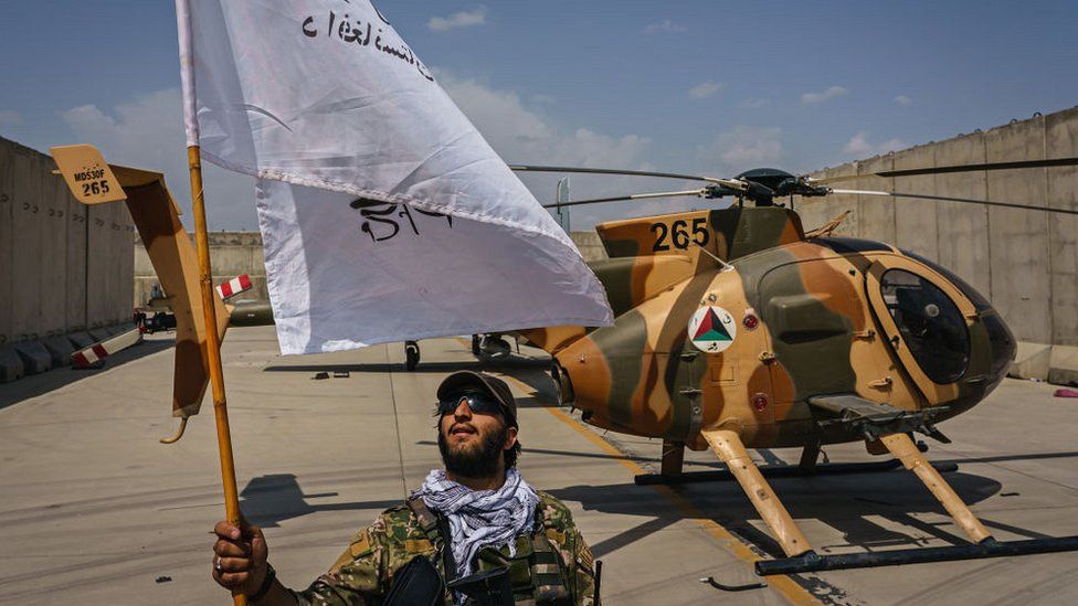 A Taliban fighter raises a flag on the military airbase side of the Hamid Karzai International Airport