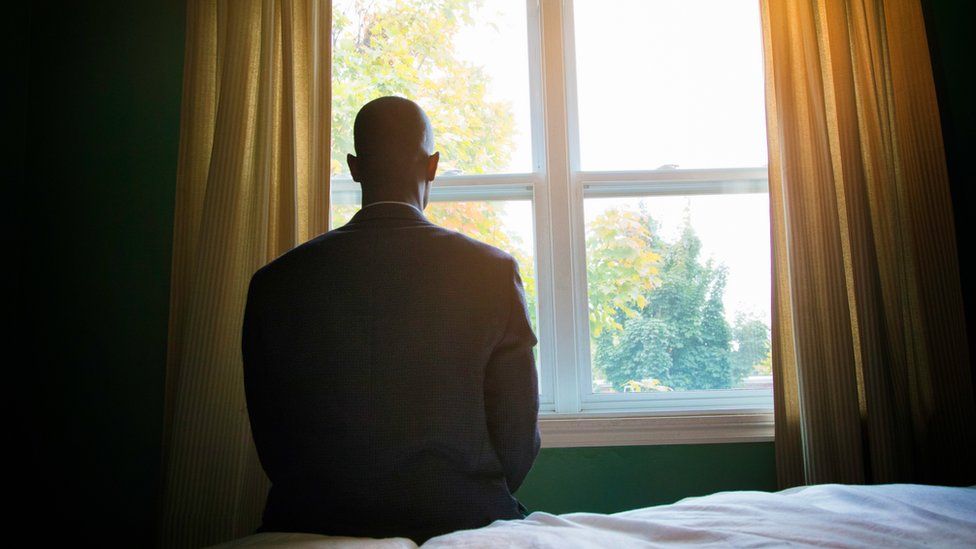 A man sitting on a bed looking out a window