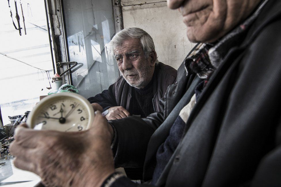 A duo of clock and watch repairmen work in their small metal shop