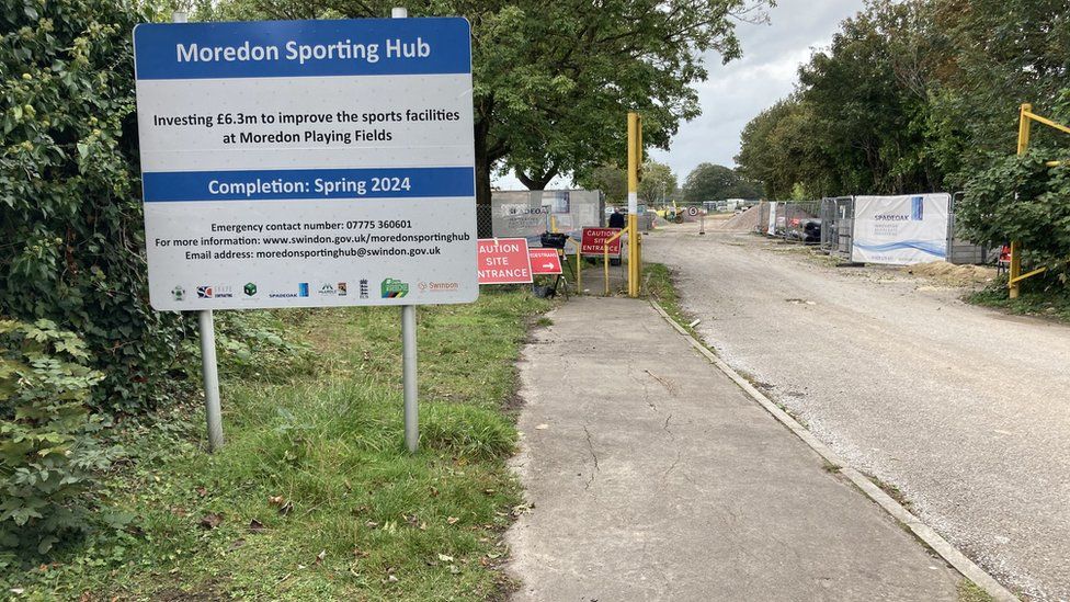 The entrance to a construction site with a sign announcing it is the Moredon Sporting Hub.
